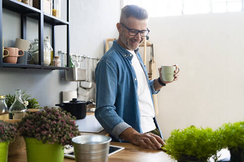 Lächelnder Mann mit Kaffeetasse in der Hand in der Küche stehend - GIOF13890