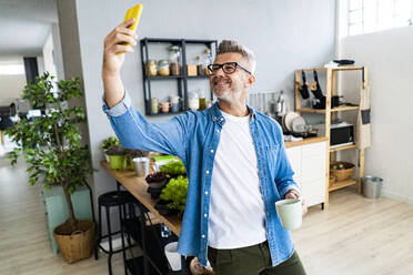 Mann mit Kaffeetasse nimmt Selfie durch Smartphone zu Hause - GIOF13896