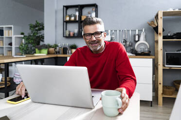 Man sitting with laptop and coffee cup at table - GIOF13904