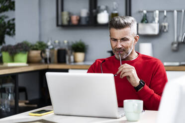 Mann mit Brille bei der Benutzung eines Laptops zu Hause - GIOF13910