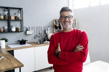 Smiling mature man with arms crossed standing in kitchen - GIOF13919