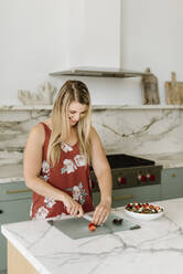 Female nutritionist cutting strawberry at kitchen counter - SMSF00562