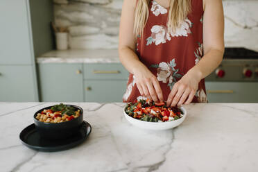 Ernährungsberaterin garniert Teller mit gehackten Erdbeeren am Küchentisch - SMSF00566