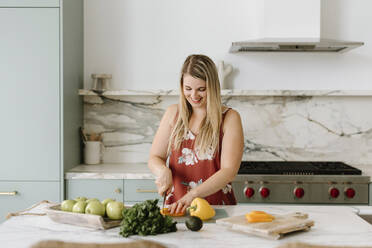 Smiling female nutritionist cutting vegetable in kitchen - SMSF00587