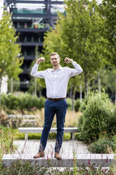 Businessman flexing muscles while standing on bench - WPEF05372