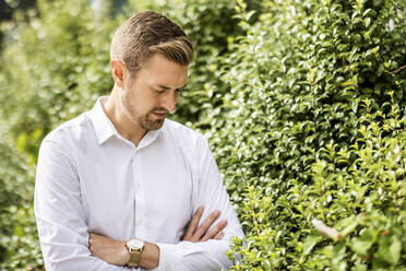 Businessman with arms crossed standing by plant in park - WPEF05373