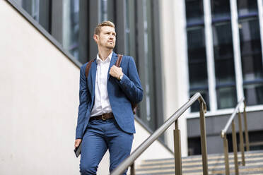 Male professional with backpack walking down on steps - WPEF05383