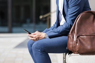 Male professional using mobile phone while sitting by backpack - WPEF05400