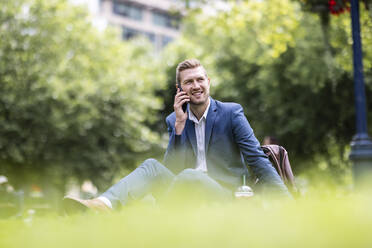 Lächelnder Geschäftsmann, der im Park mit seinem Handy telefoniert - WPEF05410