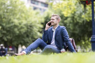 Lächelnde männliche Fachkraft, die im Park mit einem Smartphone spricht - WPEF05411