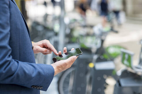 Junger männlicher Berufstätiger, der sein Smartphone an einer Fahrradabstellanlage benutzt - WPEF05433