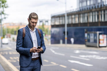 Männlicher Berufstätiger, der ein Smartphone auf einer Straße in der Stadt benutzt - WPEF05435