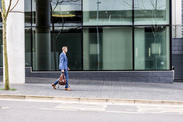 Businessman carrying backpack while walking on footpath - WPEF05441