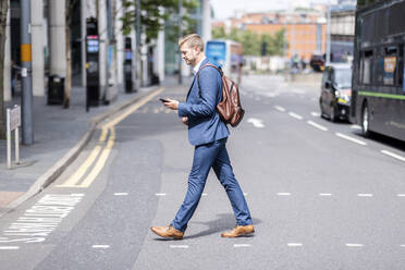 Businessman using mobile phone while crossing road - WPEF05451