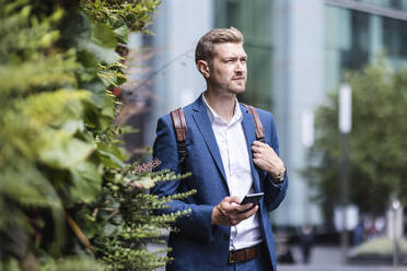 Junger Geschäftsmann hält Mobiltelefon neben Grünpflanzen - WPEF05454