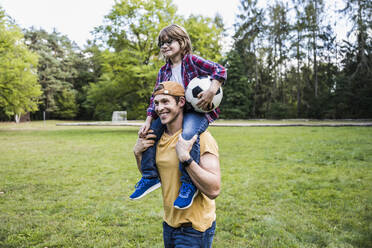 Smiling father carrying son on shoulders at park - UUF24858