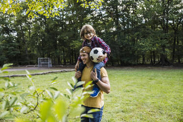 Smiling man carrying son on shoulders at park - UUF24860