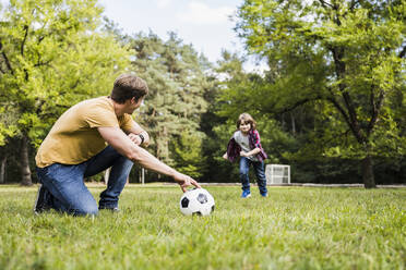 Man and boy playing with soccer ball on grass - UUF24874