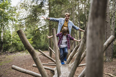 Father and son with arms outstretched walking on tree trunk - UUF24876