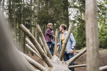 Vater schaut auf seinen Sohn, der auf einem Baumstamm im Wald steht - UUF24878