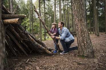 Junge hilft seinem Vater beim Aufbau eines Blockzeltes im Wald - UUF24879