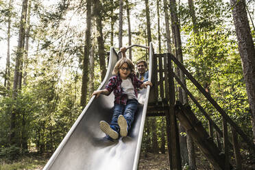 Father and son sliding on slide in forest - UUF24889