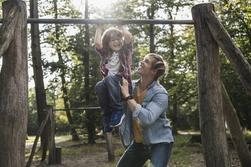 Vater hilft seinem Sohn beim Aufhängen an einem Spielgerät im Park - UUF24895