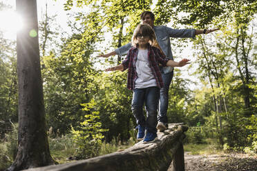 Man and boy with arms outstretched walking on log in forest - UUF24898