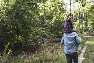 Junge mit Stock auf den Schultern eines Mannes im Wald sitzend - UUF24899