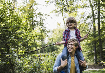 Glücklicher Vater trägt seinen Sohn im Wald auf den Schultern - UUF24900