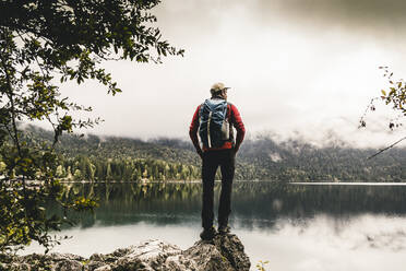 Male hiker with hands in pockets looking at lake in forest - UUF24918