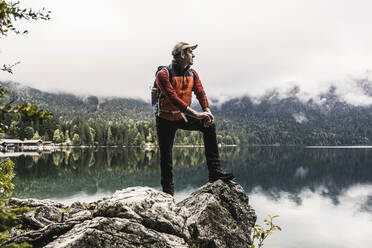 Man with backpack looking at lake while standing on rock - UUF24920