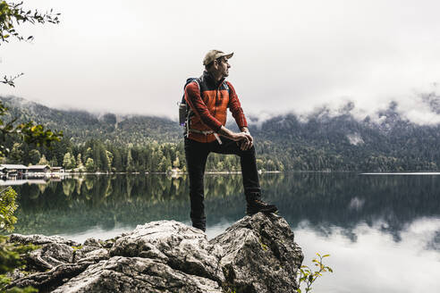 Mann mit Rucksack schaut auf den See, während er auf einem Felsen steht - UUF24920
