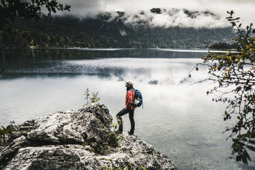 Male backpacker looking at lake in forest - UUF24923