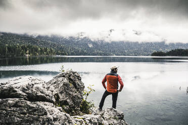 Man with hands on hip standing on rock by lake - UUF24924