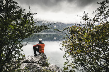 Male hiker sitting on rock by lake in forest - UUF24925