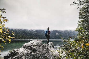 Female backpacker standing on rock by lake - UUF24928