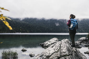Female backpacker standing on rock at lakeside - UUF24929