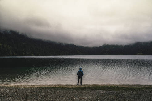 Männlicher Wanderer mit Hand in der Tasche am See stehend - UUF24930