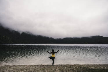 Mature woman with arms outstretched practicing yoga at lakeshore - UUF24935