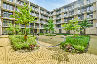 Brick walkway going between green trees and plants in inner yard of modern condominium building - ADSF31195