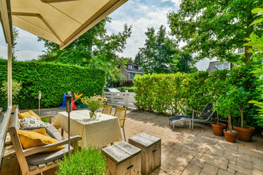 Blumenstrauß aus frischen Blumen in Vase auf dem Tisch auf der Terrasse zwischen grünen Pflanzen in sonnigen Tag platziert - ADSF31196