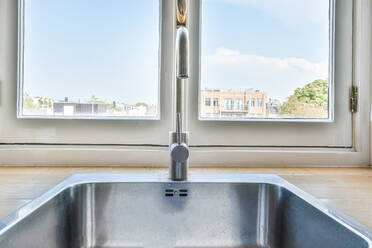 Arbeitsplatte aus Holz mit verchromtem Wasserhahn in der Nähe des Fensters mit Blick auf die Stadt unter blauem Himmel bei Tageslicht - ADSF31201