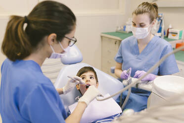 Hoher Winkel des Zahnarztes und der Assistentin, die die Zähne eines Jungen während eines Eingriffs in einer Zahnklinik behandeln - ADSF31214