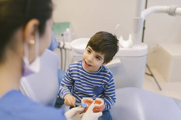 Lächelnde Kieferorthopädin, die einem Patienten mit Zahnbürste das Zähneputzen am Kiefermodell in einer Zahnklinik beibringt - ADSF31215