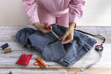 Anonyme Näherin beim Zuschneiden einer Jeanstasche auf einem Holztisch im Atelier mit einer Schere - ADSF31229