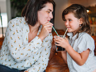 Lächelndes Mädchen teilt sich ein Glas süße Limonade mit ihrer Mutter und trinkt mit einem Strohhalm in einem Café - ADSF31263