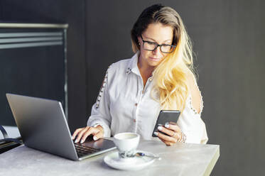 Blond businesswoman using mobile phone while working in cafe - PGF00848