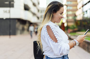 Smiling female freelancer using mobile phone on footpath - PGF00853