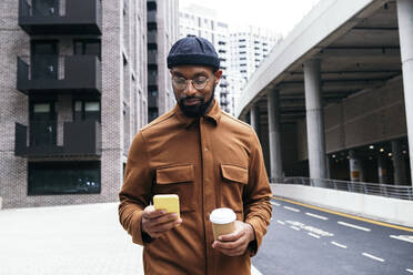 Man using mobile phone while having coffee in city - ASGF01630